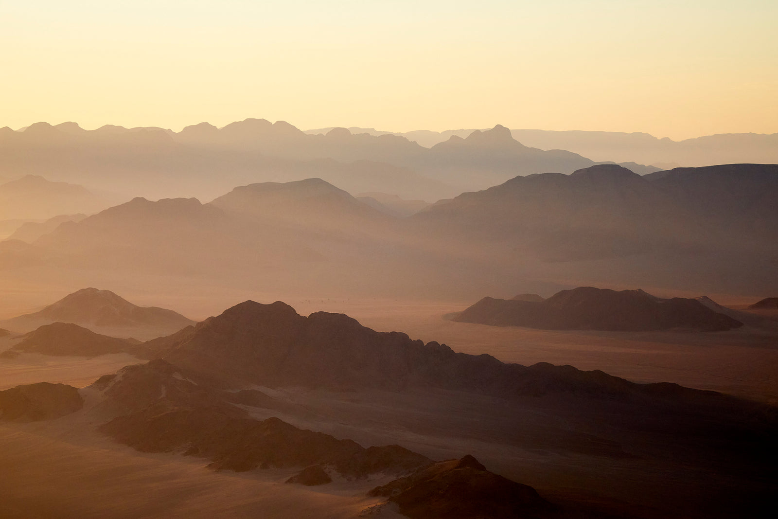Aerial view of layered mountain ridges receding into golden dawn haze, Namibian desert