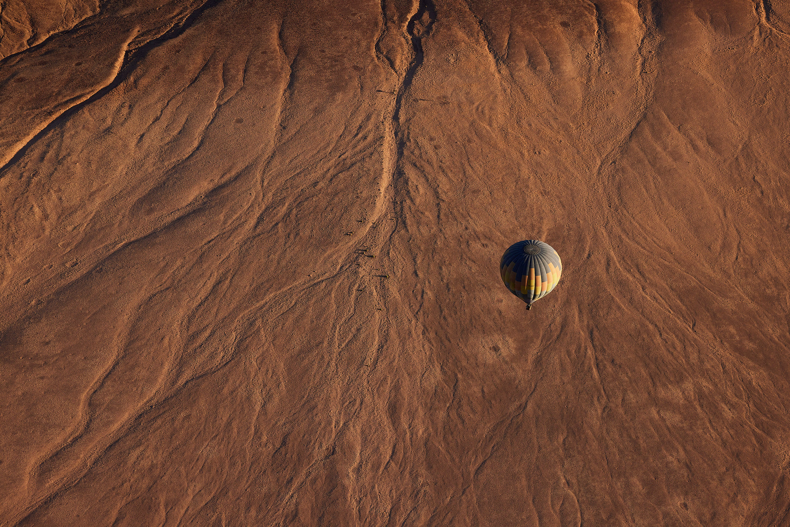 Aerial view of a hot air balloon casting a shadow over textured red-brown desert terrain