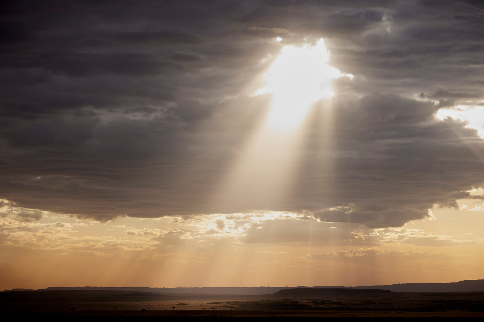 Single shaft of golden light breaking through dark storm clouds over open plains