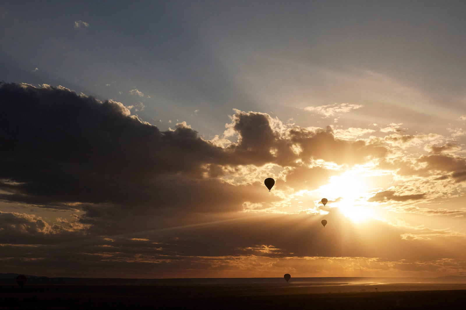 Four hot air balloon silhouettes floating against a dramatic sunset sky over open plains