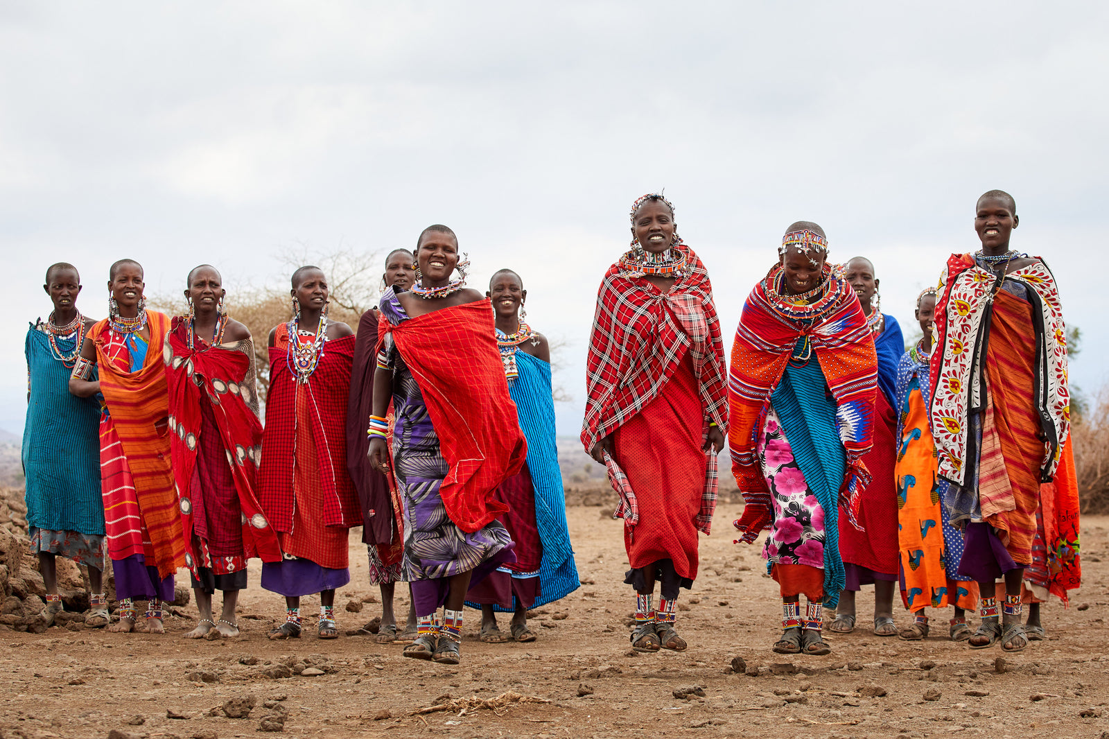 Large group of Maasai women jumping and dancing together in vibrant red and blue shukas