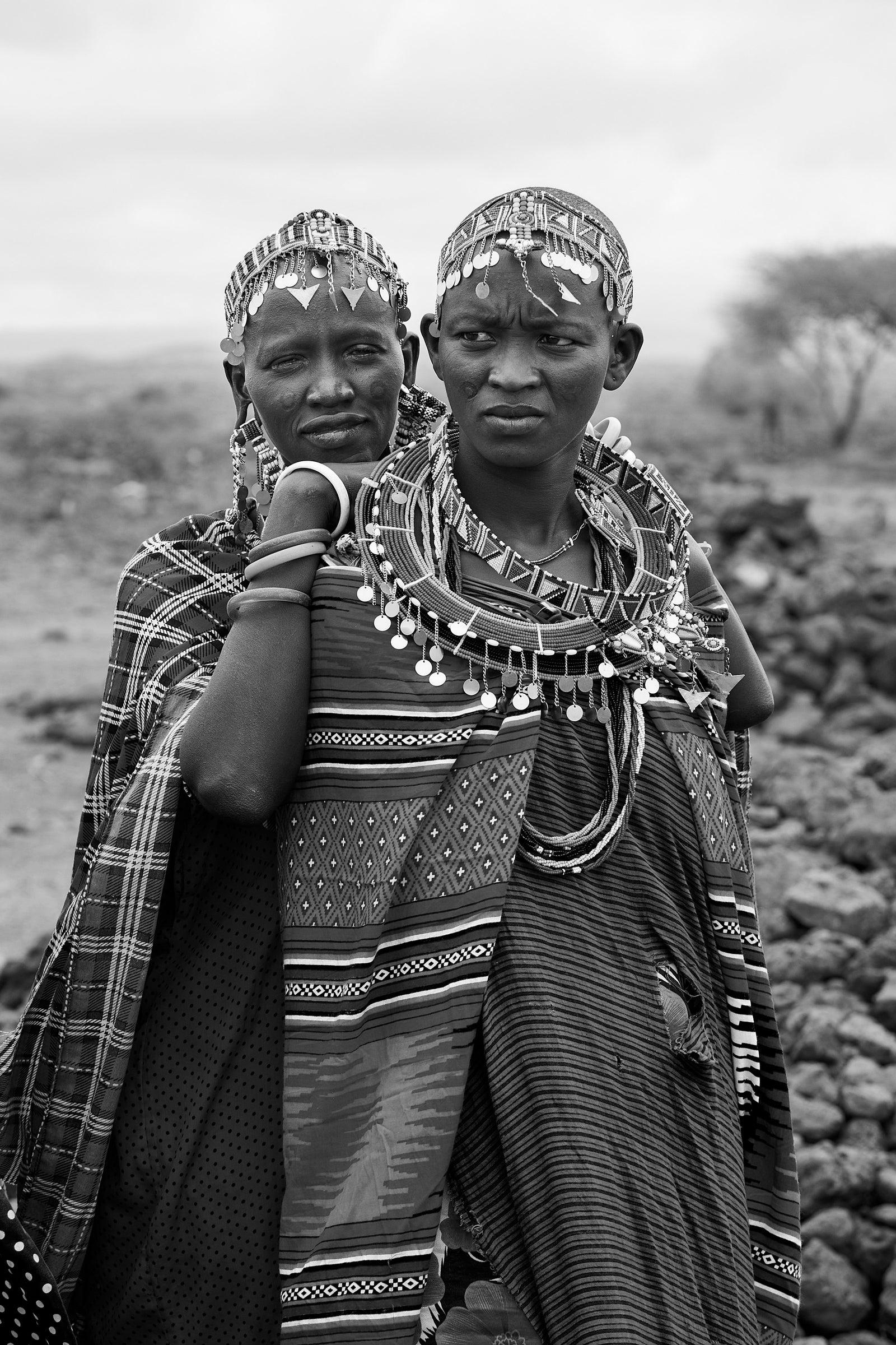 Black and white portrait of two Maasai women standing close together wearing beaded headpieces and layered necklaces