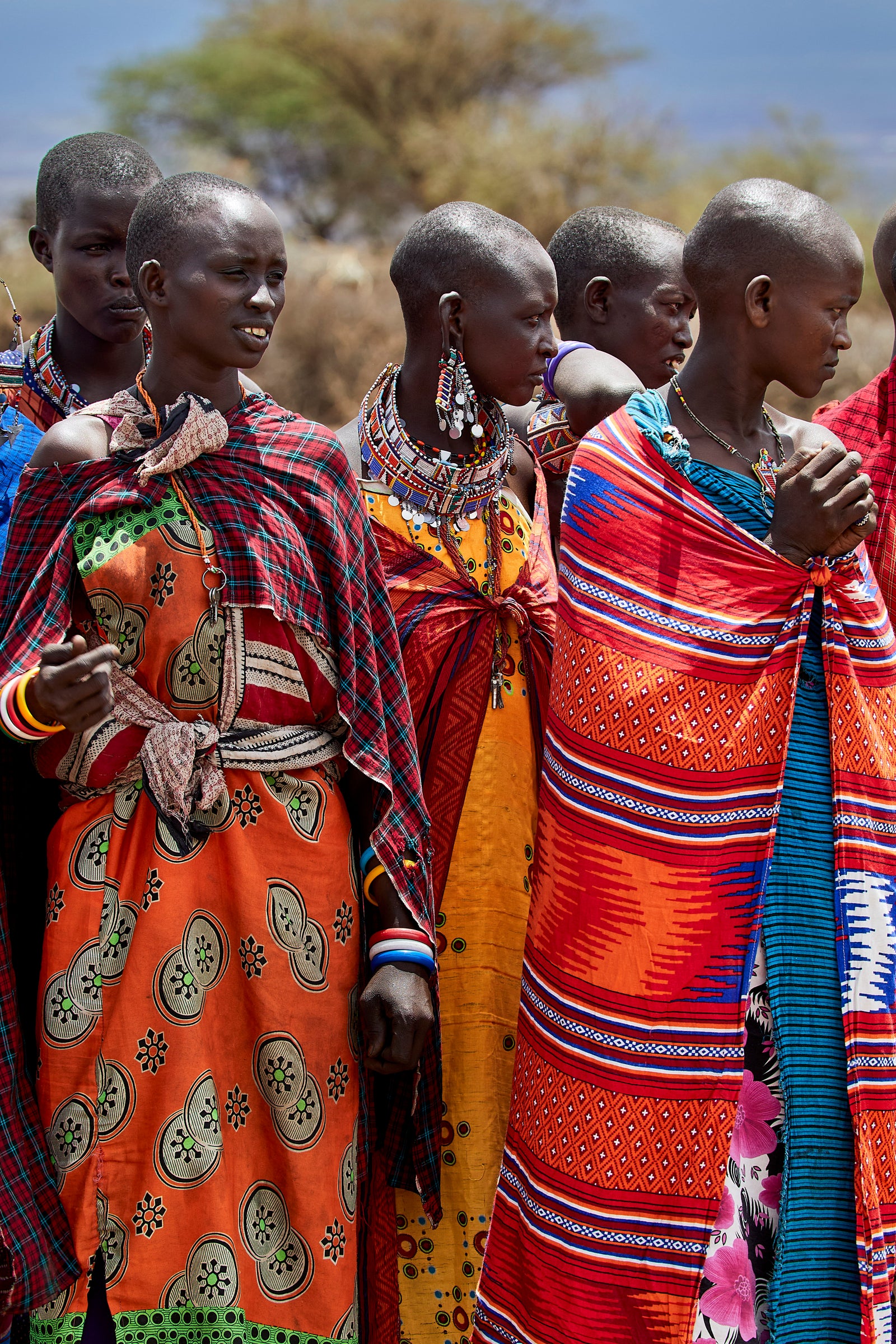 Group of young Maasai women standing together in brightly patterned wraps and beaded necklaces