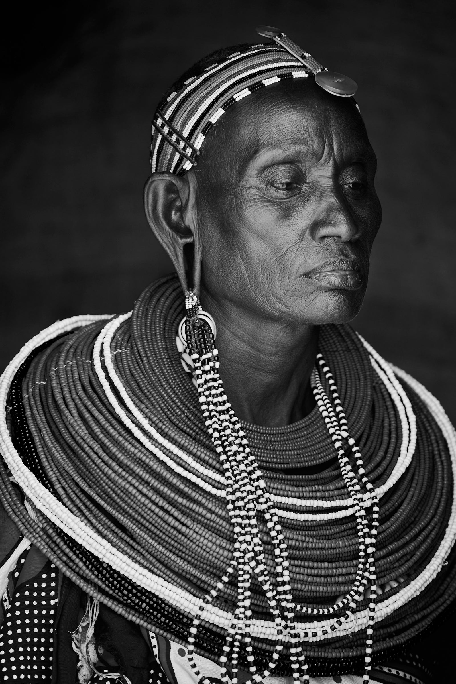 Black and white portrait of an elder Samburu woman in profile, wearing stacked beaded necklaces and headpiece