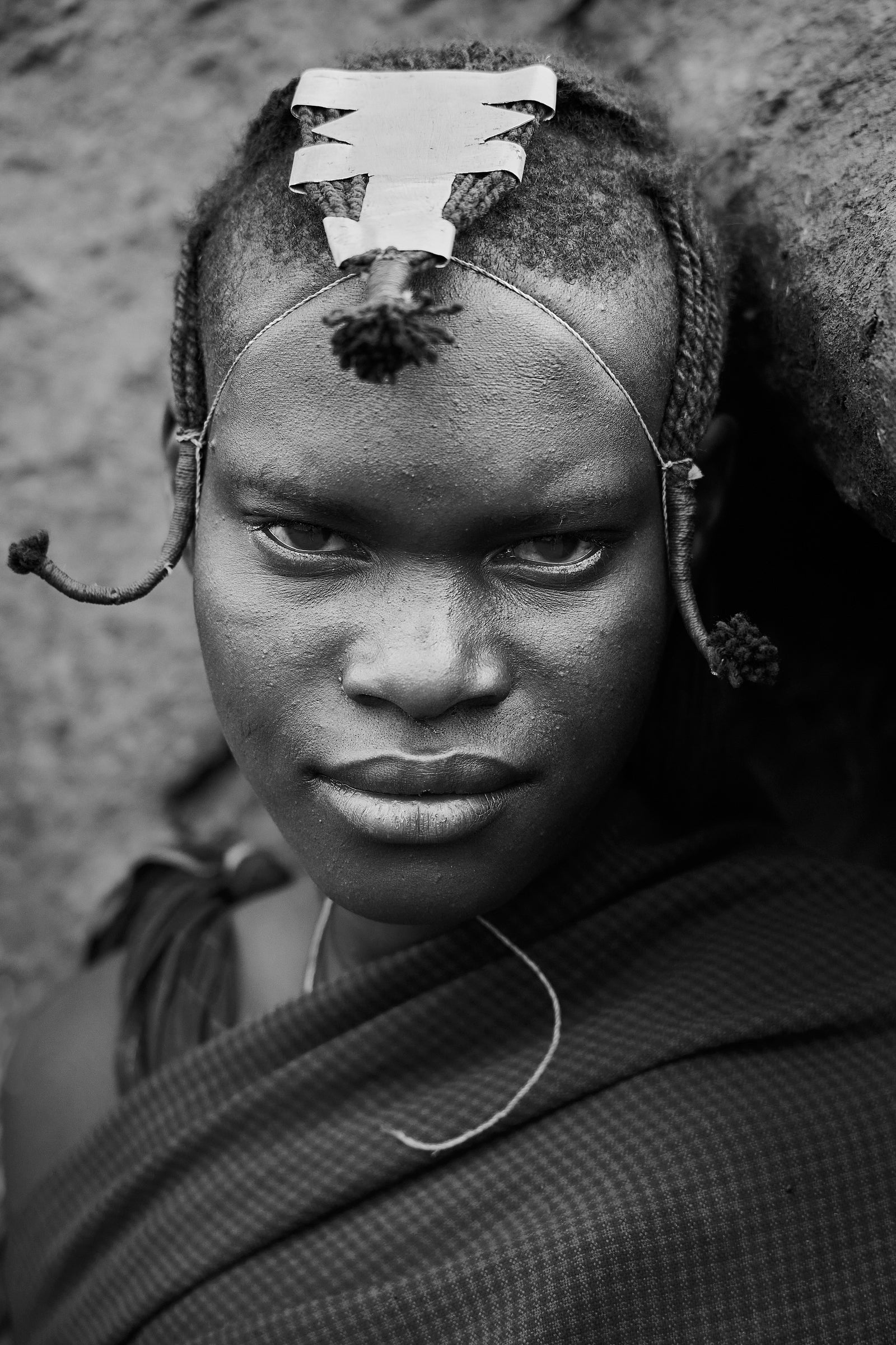 Black and white close-up portrait of a young Maasai woman looking directly at camera, braided hair and metal hair clip
