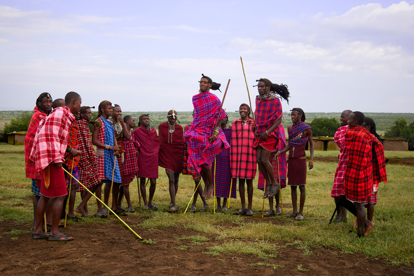 Group of Maasai warriors performing a traditional jumping dance in colourful checked shukas on green grass