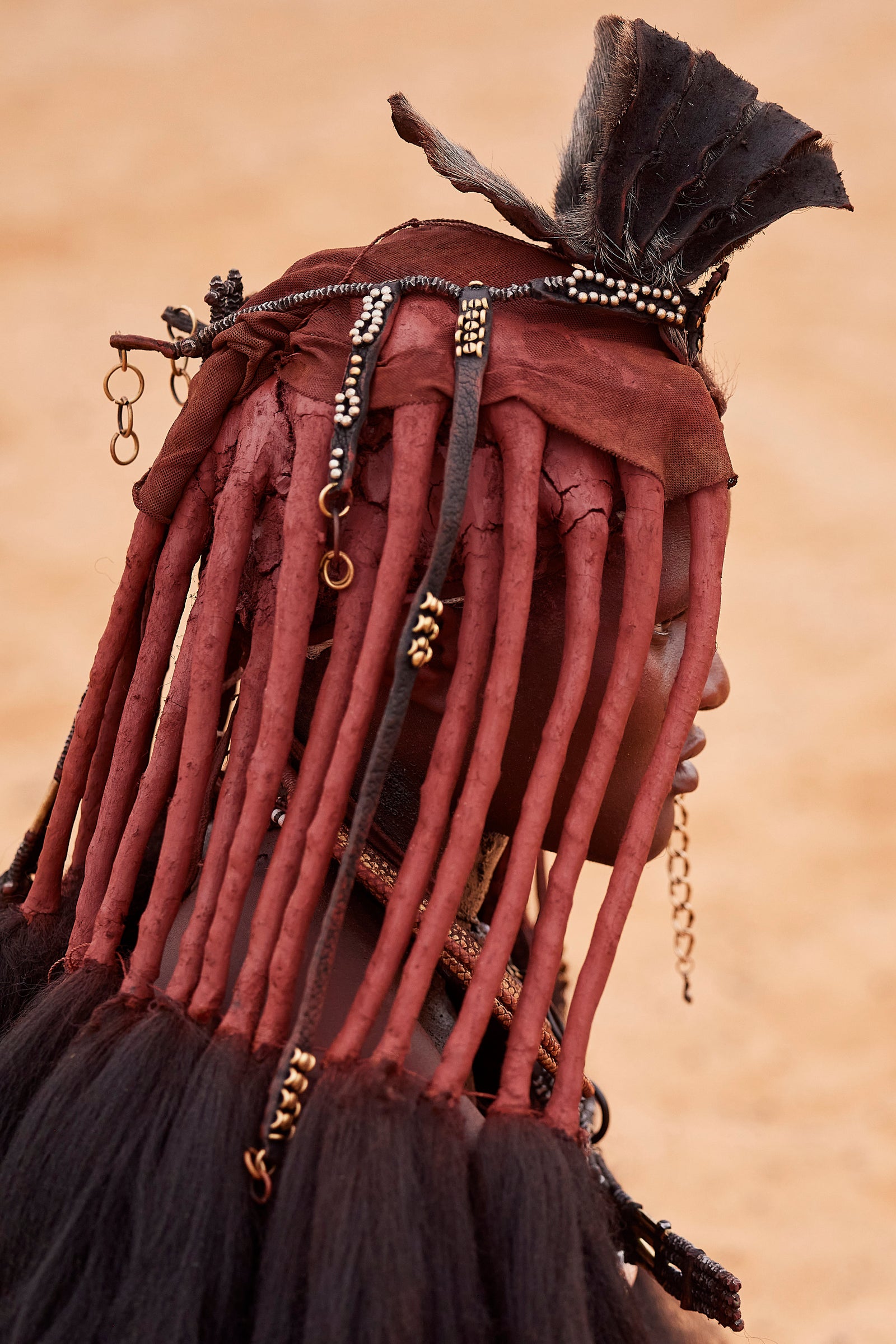 Rear view of a Himba woman's ochre-coated braids adorned with beads, chains, and a leather headpiece